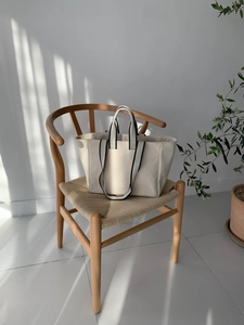 Beige canvas tote bag with black striped straps on a stylish wooden woven chair