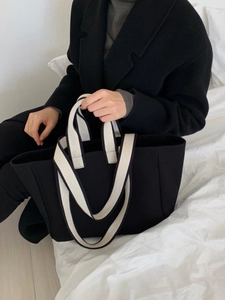 Detailed view of a black canvas tote bag with contrast webbing straps on white bedding