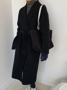 Detail of a minimalist black wool coat with tie-waist and matching black tote bag