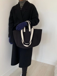 Detail of minimalist black canvas tote bag with striped handles held by model