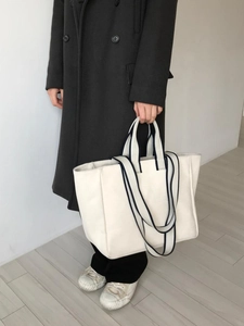 Detail of a beige canvas tote bag with dark blue striped straps and dual handle design