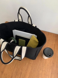 Top view of spacious canvas tote bag with black body and beige handles on wood table