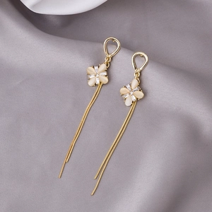 Detailed view of gold clover earrings with cat eye stones and long tassel chains on silk