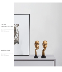 Detail of two luxury matte gold abstract face sculptures on black circular bases
