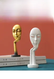 Close-up of golden and white abstract face sculptures on books against orange background