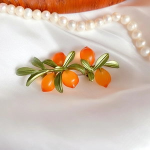 Detail of vintage orange glass brooch with green leaves on white silk background