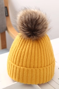 Detalle del gorro de punto amarillo para bebé con un gran pompón de piel sintética