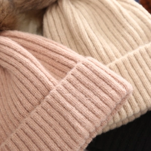 Detalle de gorros de punto rosa y beige con textura acanalada suave y pompones de piel sintética