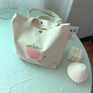 Detail der Canvas-Lunchtasche mit Pfirsichdruck und Metallverschluss auf Karodecke