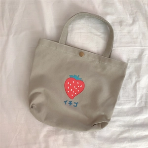 Detailansicht des Erdbeerdrucks und Metalldruckknopfs auf der beigen Canvas-Tasche