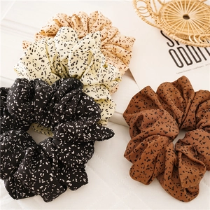 Detail of four soft oversized polka dot scrunchies in beige, black, khaki, and caramel