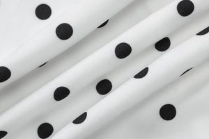 Close-up of lightweight white fabric with regular black polka dot pattern and soft texture
