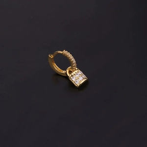 Macro view of gold key-shaped earring with clear zircons on black background