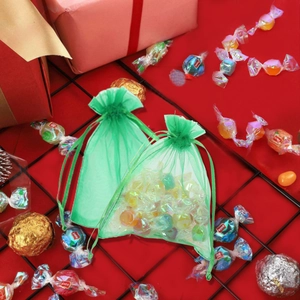 Green organza drawstring gift bags for Christmas candies shown on red gift box