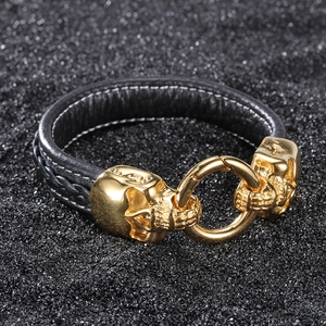 Punk black leather bracelet with dual gold skulls and lobster clasp on black sand