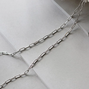 Detailed view of silver minimalist paperclip chain link over a grey stone block surface