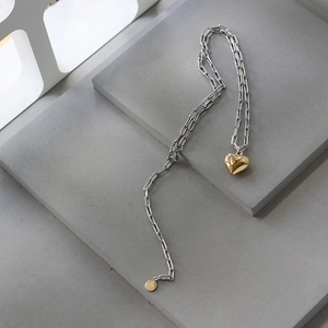 Detail of mixed-metal paperclip chain necklace with gold 3D heart pendant and logo tag