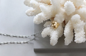 Detailed view of 3D gold heart pendant on silver rectangle link chain over coral texture