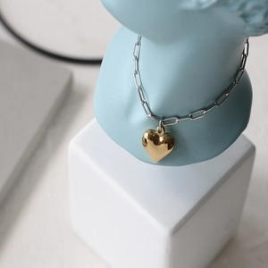 Detail of mixed-metal paperclip chain necklace with a 3D gold heart pendant on a bust