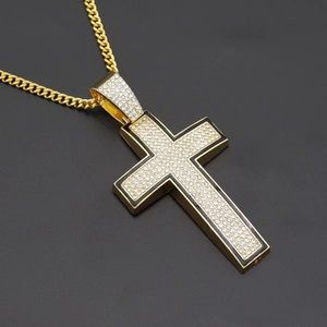Macro detail of gold cross pendant with clear crystals on cuban link chain