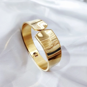 Detail view of gold-plated wide bangle with spring hinge on elegant white silk background