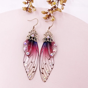 Macro shot of gradient butterfly wing earrings with sparkling rhinestones on pink decor