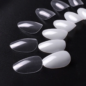Glossy almond press-on nail tips in clear and milky white colors set on dark background