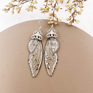 Macro detail of long silver butterfly wing earrings with glitter on a vintage background