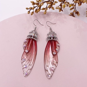 Detail of gradient red butterfly wing earrings with crystals on a pink tray