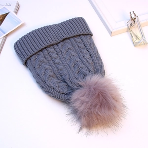 Macro shot of cable-knit grey beanie featuring a fluffy purple faux fur pom-pom detail