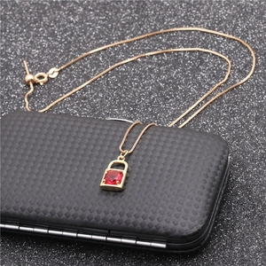 Close-up of golden necklace with a lock pendant featuring a red zircon gemstone