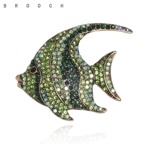 Detailed view of fish brooch with green crystals and vintage alloy base on white background