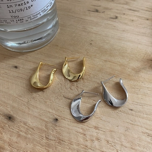 Macro view of gold and silver U-shaped twist earrings on a minimalist wooden surface
