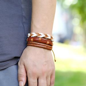 Close-up of a three-piece set of woven leather and rope bracelets worn on a male wrist