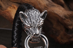 Vue macro de têtes de loup en argent et bracelet en cuir tressé noir sur bois