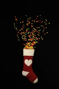Macro view of red knitted Christmas stocking with white hearts and colorful candies spilling out