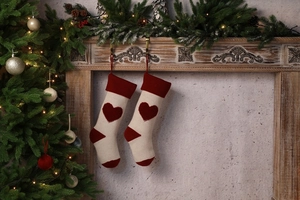 Close-up of knitted Christmas stockings with 3D red heart pattern on a wooden fireplace