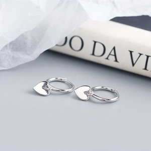 Macro shot of minimalist silver heart charm hoop earrings on a decorative book background