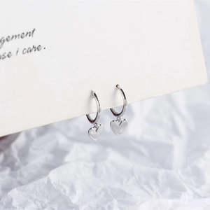 Detail view of silver heart pendant hoop earrings hanging on minimalist white card display