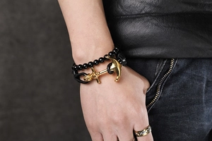 Close-up of men's leather braided bracelet with gold anchor pendant on model's wrist