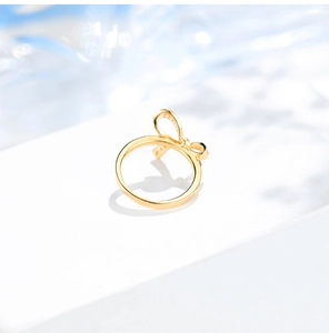 Luxury gold bow ring with baguette diamonds displayed on a white stone pedestal