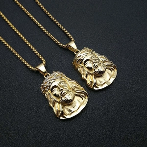 Close-up of gold Jesus head pendants with crystal accents on a grey leather surface