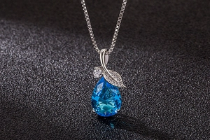 Macro shot of blue waterdrop pendant with silver leaf detailing on a box chain necklace