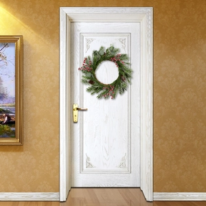 Christmas wreath with red berries and pine cones hanging on a white wooden door