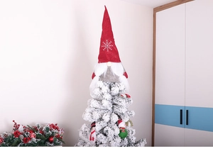 Gnome Christmas tree topper with red snowflake hat and white beard on a snow-dusted tree
