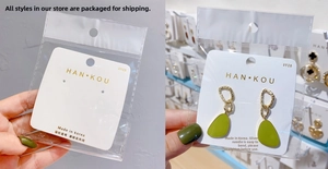 Detailed view of dark green drop earrings with gold chains on a white display card
