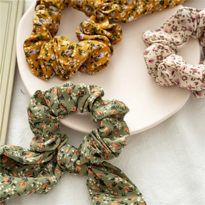 Close-up of three floral fabric hair scrunchies in yellow, green, and pink colors