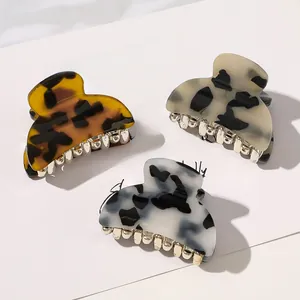 Close-up of three acrylic hair claws in amber, marble, and ink patterns with gold teeth