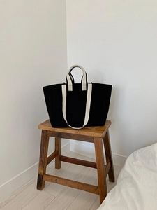 Detail of a black canvas tote bag with cream woven handles on a rustic wooden stool
