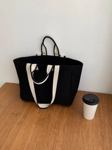 Minimalist black canvas tote bag with white straps displayed on a wooden table surface